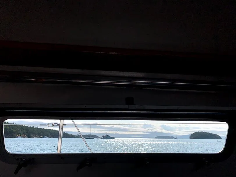 A calm anchorage with boats and islands seen through the long cabin window of a sailboat