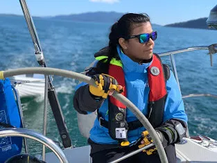 Urvashi handling lines in the cockpit under way, with forested shoreline behind